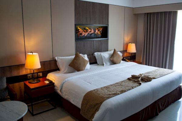 A neatly decorated hotel room with a king-sized bed, two lamps, a wall art piece, and curtains. The room looks cozy and inviting.