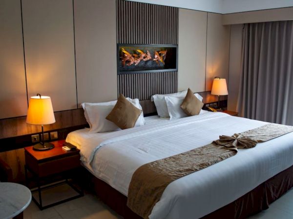 A neatly decorated hotel room with a king-sized bed, two lamps, a wall art piece, and curtains. The room looks cozy and inviting.