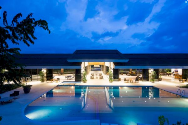 A luxurious pool area with modern architecture, surrounded by lounge chairs and lit up against a twilight sky, creating a serene ambiance.