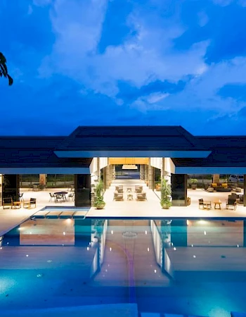 A luxurious building with an illuminated pool and seating area is shown under a twilight sky.