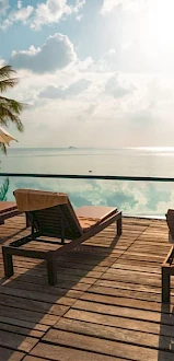 A serene poolside deck with lounge chairs and umbrellas overlooking a vast body of water under a partly cloudy sky.