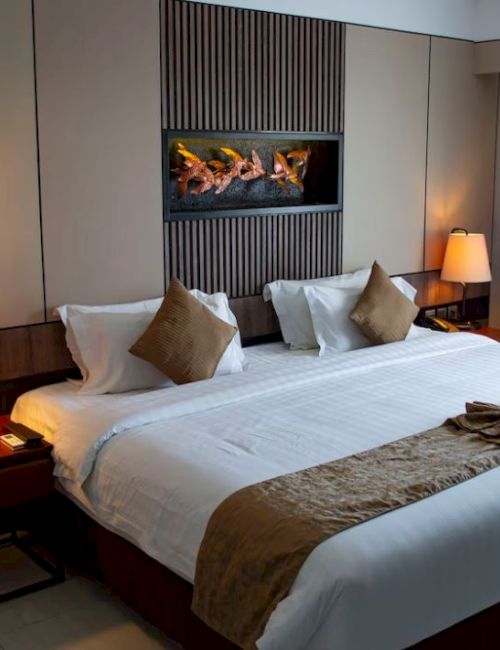 A cozy hotel room with a king-size bed, decorative pillows, bedside lamps, wall art, and a window with curtains for a comfortable stay.