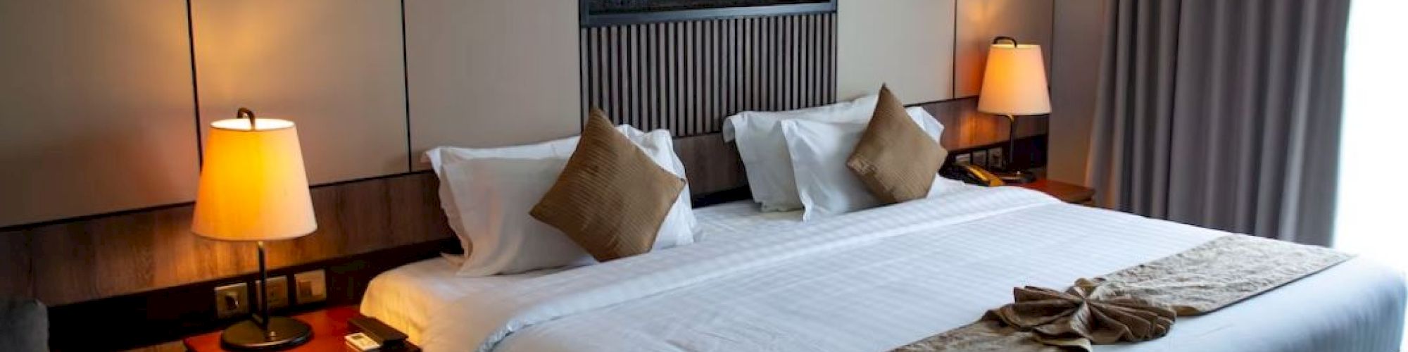 A cozy hotel room with a large bed, decorative pillows, bedside tables with lamps, and a modern wall feature above the bed.