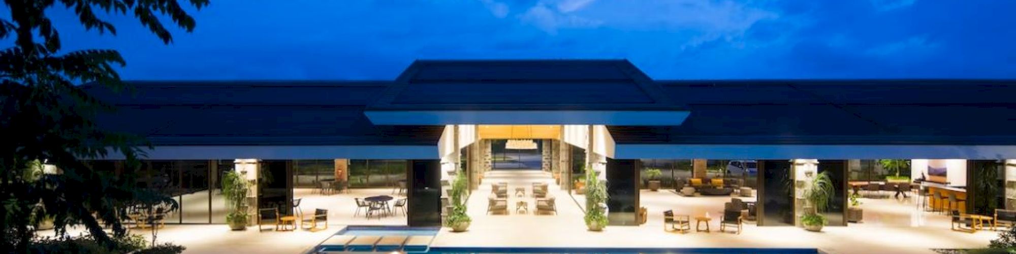 A modern building with an illuminated pool and open seating area, set against a blue sky backdrop at dusk, creating a serene ambiance.
