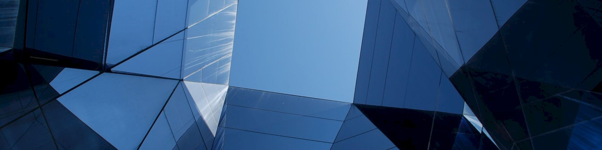 Geometric architectural structure with reflective glass surfaces forming a tunnel-like view toward the sky.