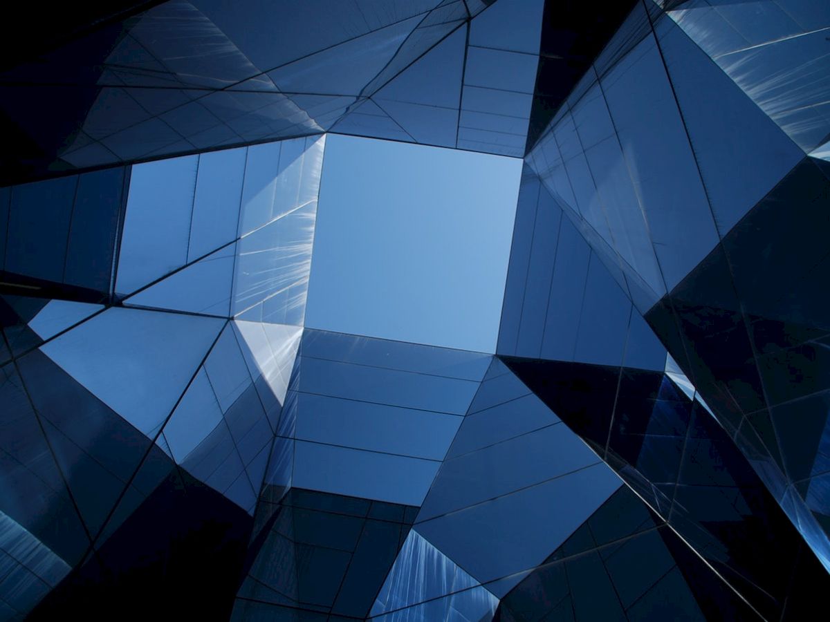 Abstract view of a modern glass building with reflective surfaces, creating geometric patterns against a clear blue sky.