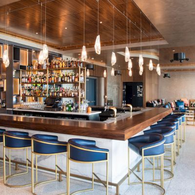 A modern bar with navy stools, overhead lights, and a well-stocked counter; the room has a stylish and inviting atmosphere.