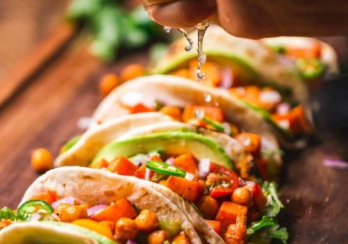 Tacos filled with chickpeas, avocado, red onions, and cilantro. A hand squeezes lime juice over them.