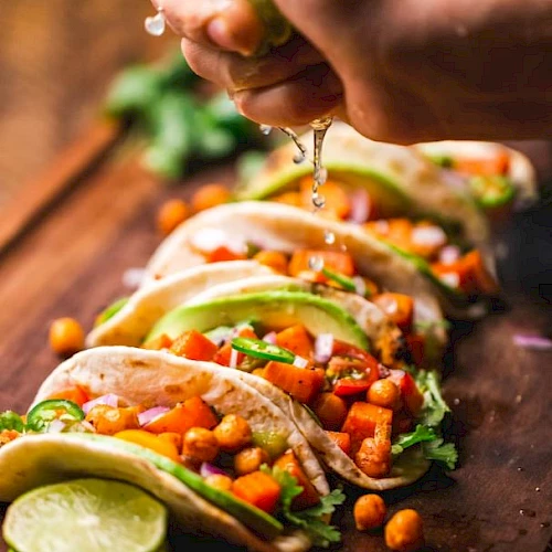 Tacos filled with chickpeas, avocado, red onions, and cilantro. A hand squeezes lime juice over them.