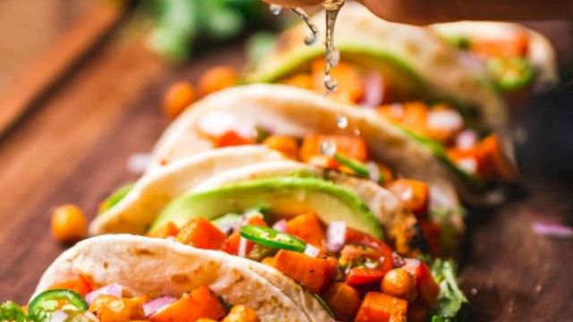 Tacos filled with chickpeas, avocado, red onions, and cilantro. A hand squeezes lime juice over them.