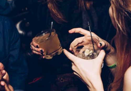 People are enjoying drinks and laughing, captured in a lively moment with hands holding glasses and showing expressions of amusement.
