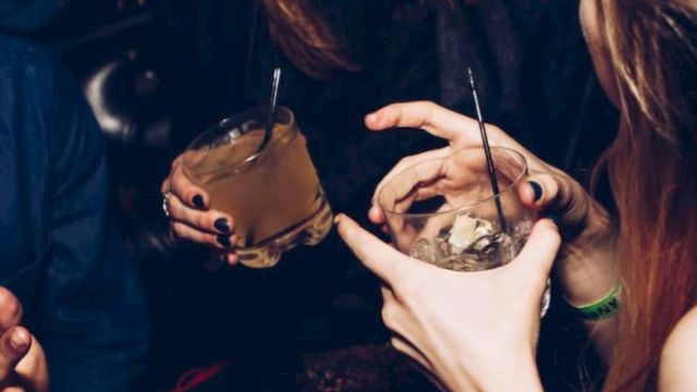 People are enjoying drinks and laughing, captured in a lively moment with hands holding glasses and showing expressions of amusement.