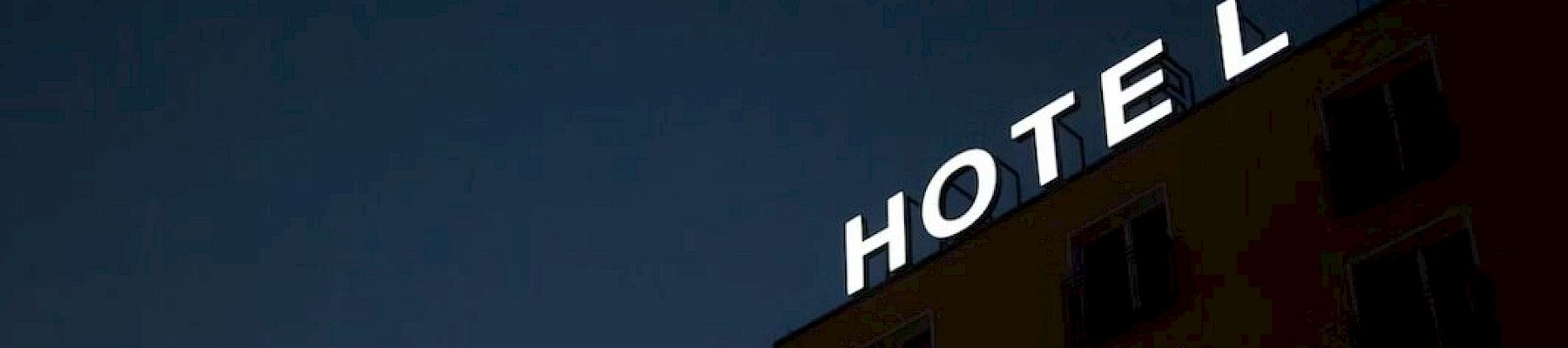 The image shows a dark building at night with illuminated letters spelling "HOTEL" on top, with the "L" slightly separated.