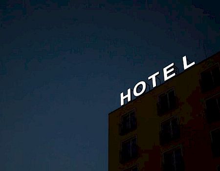 The image shows a dark building at night with illuminated letters spelling "HOTEL" on top, with the "L" slightly separated.