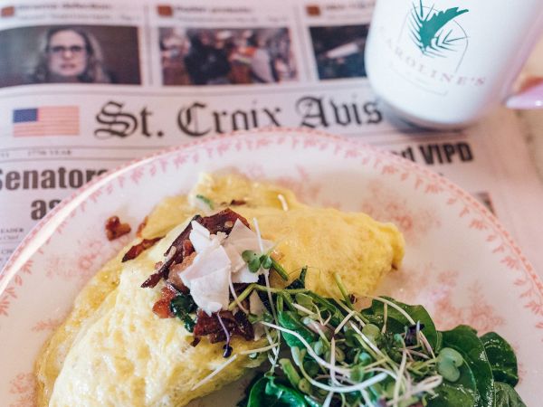 A plate with an omelette topped with greens, alongside a newspaper and a coffee mug.