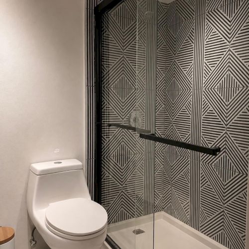 A modern bathroom with a toilet and a glass shower, featuring bold geometric black-and-white tile patterns.