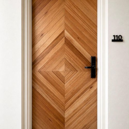A modern wooden door with a herringbone pattern, black handle and lock, and the number 110 by the frame.