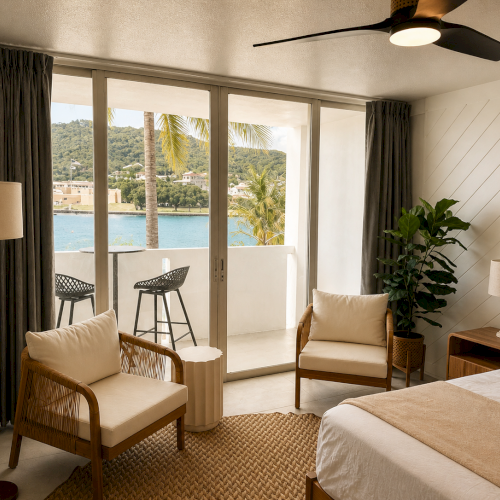 Bright seaside room with big glass doors, curtains, patio chairs, a ceiling fan, lamps, and a view of green hills.