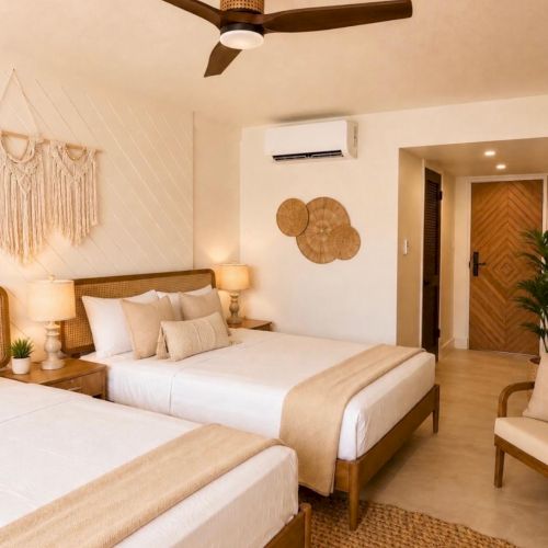 A bright twin bedroom with two beds, a ceiling fan, wall art, an air conditioner, and warm wood door accents.