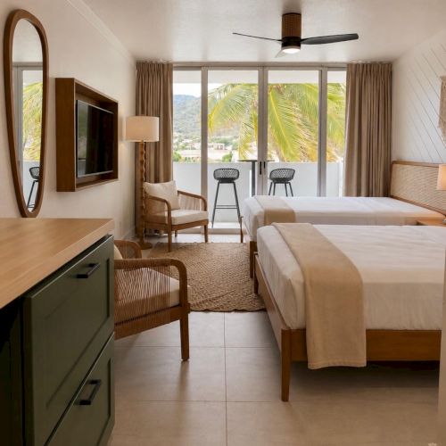 A bright hotel bedroom with two beds, a ceiling fan, matching curtains, and palm-tree views through large sliding doors.
