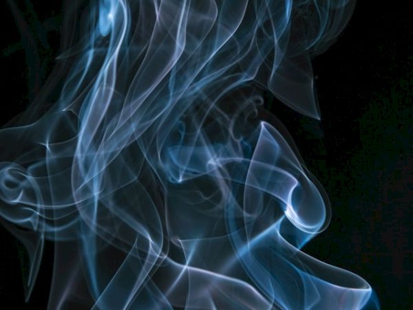 Wisps of blue smoke swirl gracefully against a dark background, creating an ethereal and mesmerizing visual effect.