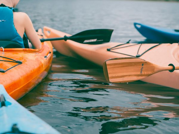 The image shows three kayaks on water, with paddles and a person wearing a life vest. The scene is calm and recreational.
