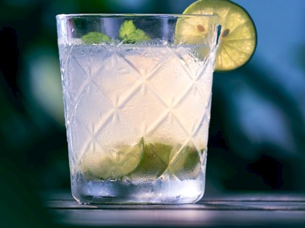 A glass with a lime-based drink, garnished with lime slices, sits against a blurred green background.
