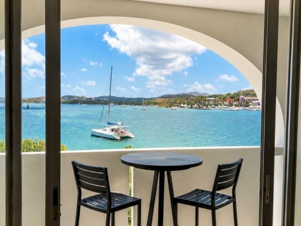 Balcony with two bar stools overlooking a turquoise bay with sailboats under a blue sky.