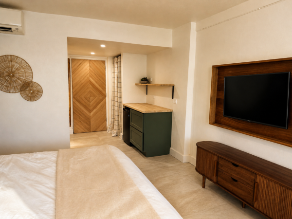 A modern bedroom shows a white bed, wall TV, dark-green vanity, and a doorway with curtains.