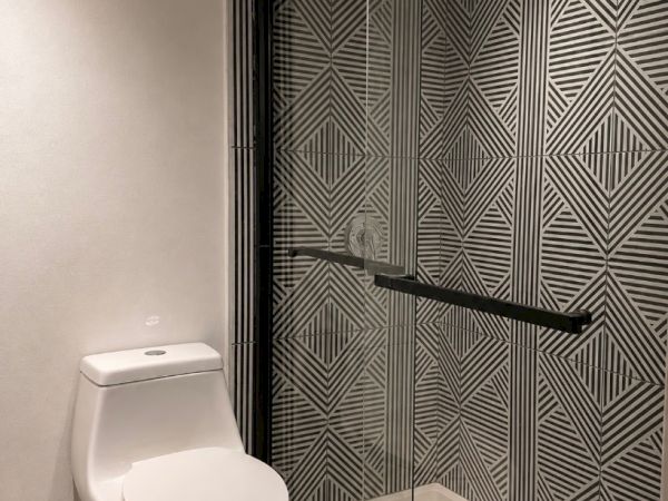 A modern bathroom with a toilet and a glass-enclosed shower featuring bold geometric tile patterns and a black grab bar.