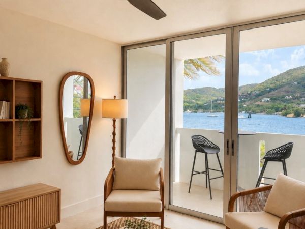 A bright modern living room with wood furniture, woven rug, a ceiling fan, and large sliding doors revealing a lakeside view.