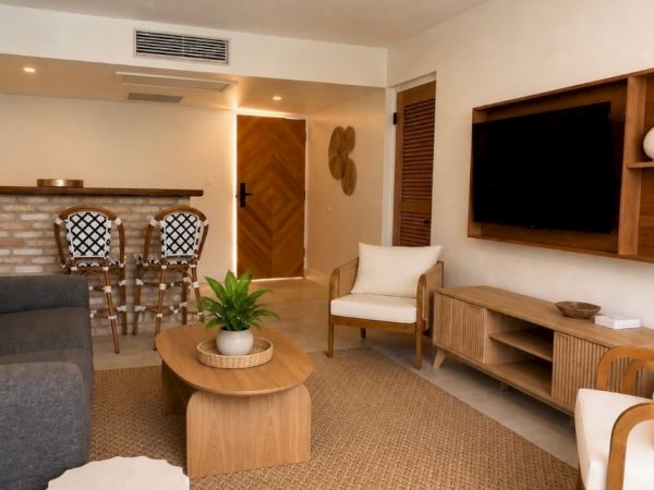 A modern living room with a ceiling fan, TV console, armchairs, and a round wooden coffee table.