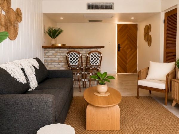 A cozy living room with a wood ceiling fan, dark sofa, armchairs, a round coffee table, and warm light through large walls.