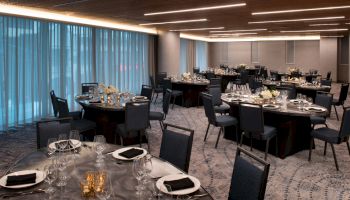 The image shows an elegantly set banquet hall with round tables, chairs, and dinnerware under soft lighting with blue curtains.