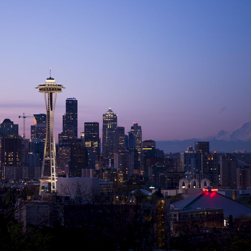 City skyline at dusk with a prominent tower and mountain in the background.