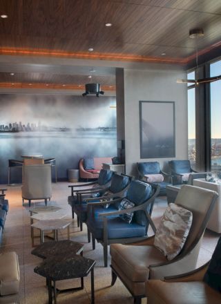 A modern lounge with comfortable seating, large windows offering a scenic view of the water and skyline, and ambient lighting creates a cozy atmosphere.